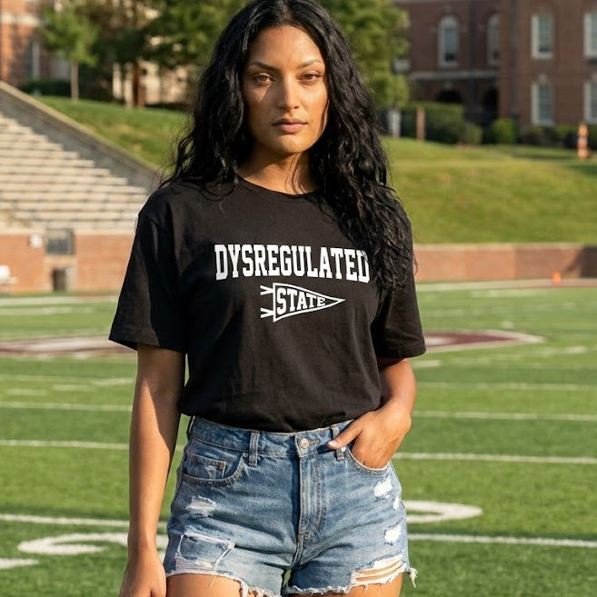 Person wearing a black t-shirt with 'DYSREGULATED STATE' text on a grassy field.