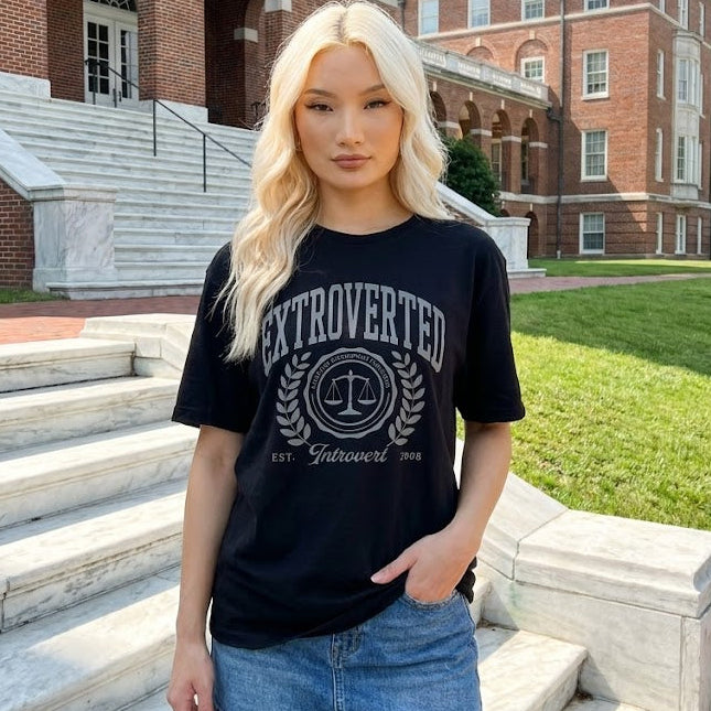 Person wearing a black t-shirt with 'EXTROVERTED' text, standing on steps in front of a brick building.