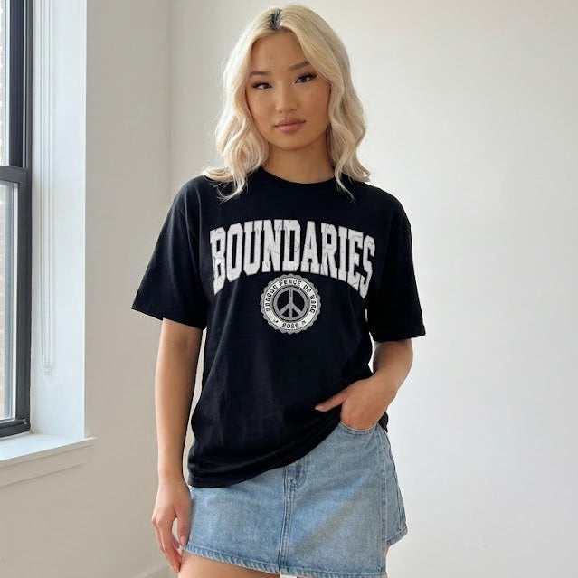 Person wearing a black 'BOUNDARIES' t-shirt with a peace symbol indoors.