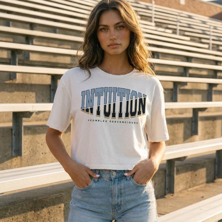 Woman wearing a white t-shirt with 'INTUITION' printed on it, standing in front of empty bleachers.